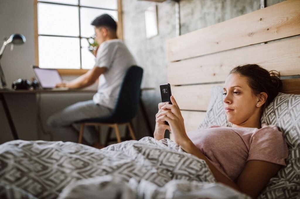 Couple in bedroom, Girl is lying on bed and the boy is working on laptop